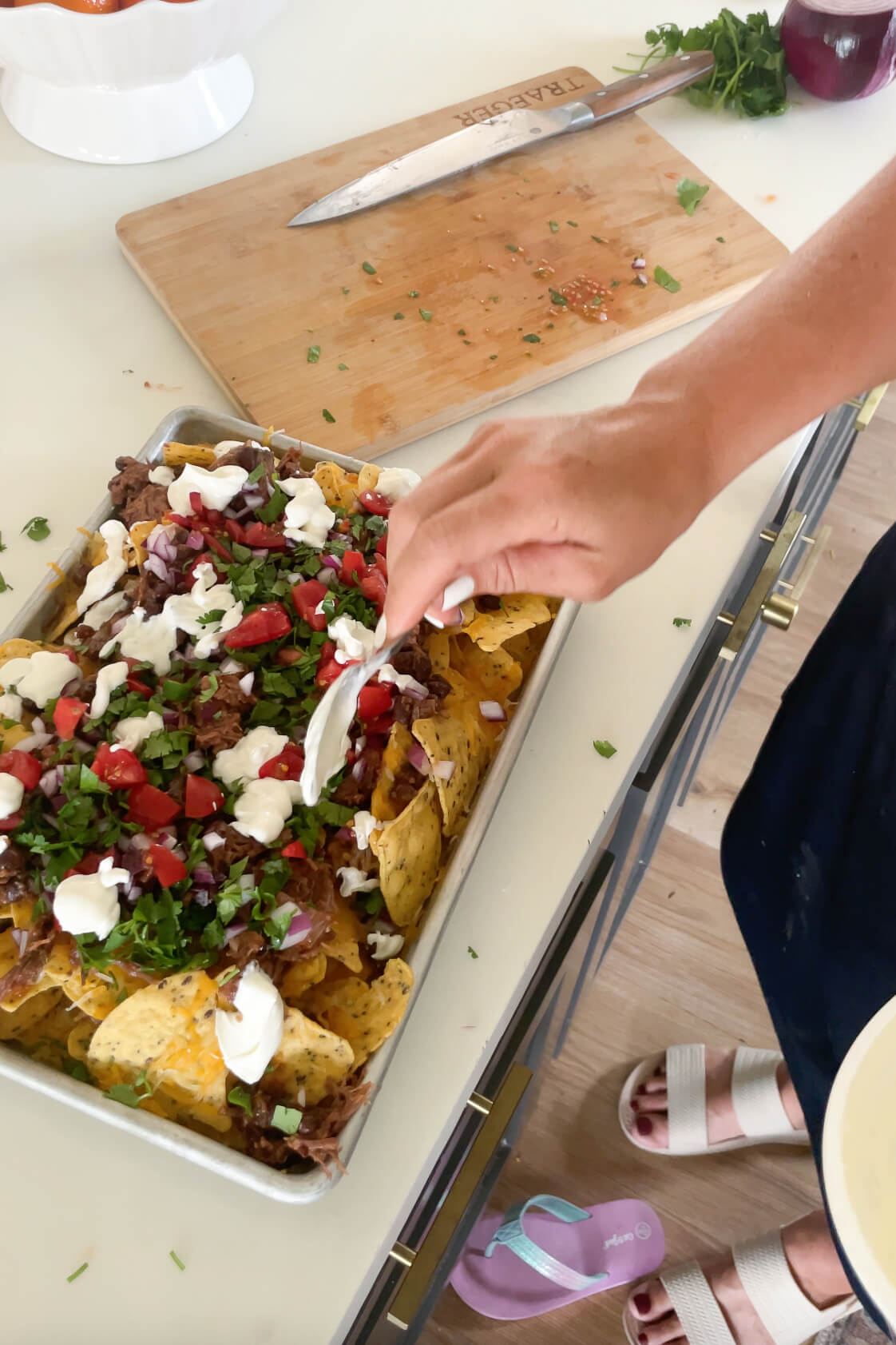 Dropping sour cream onto the finished sheet pan nachos.